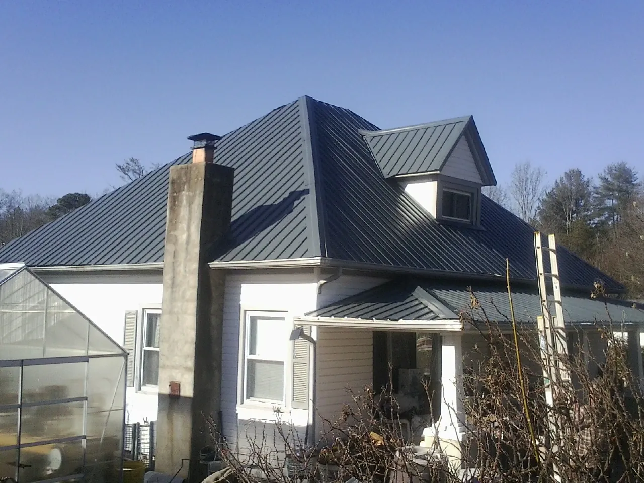 Dark blue standing seam metal roof on a white farmhouse with dormer — Slate & Tile Roof Repair by Roofing Brothers in Mc Alpin