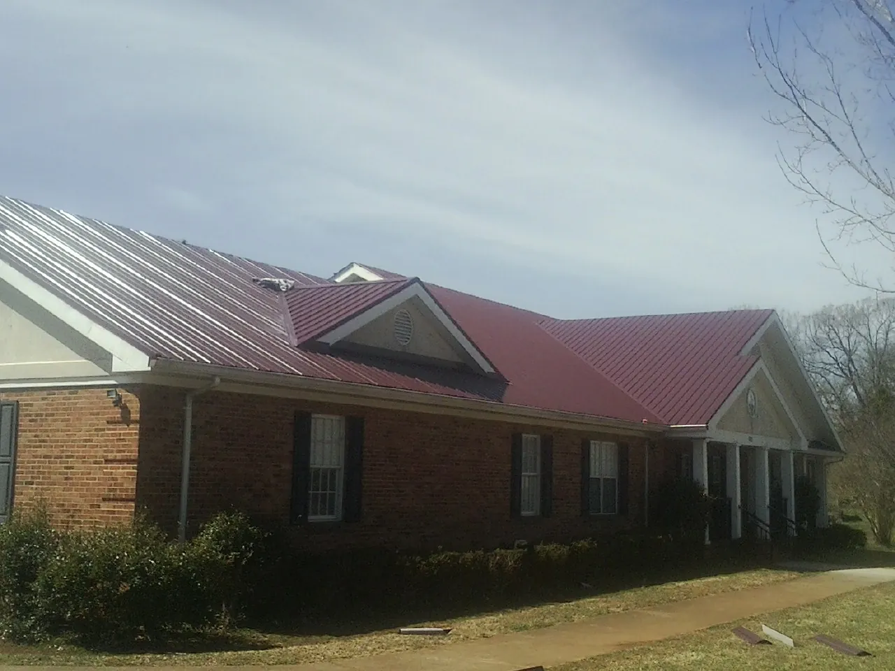Red metal roof with gabled entries on a long brick building, from a Hail Damage Roof Repair job in Mc Alpin