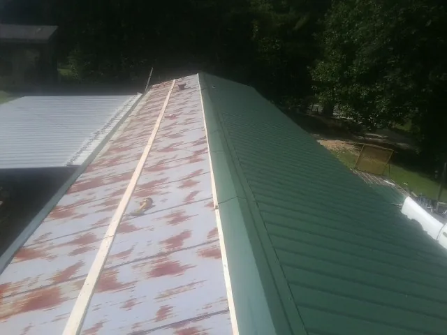 Old rusted panels beside newly installed green metal roofing — Wind Damage Roof Repair by Roofing Brothers in Mc Alpin
