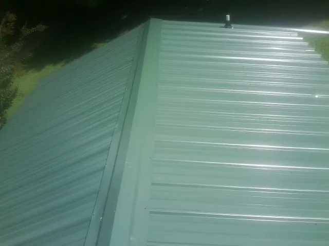 New green metal panels meeting at the ridge of a roof — Flat Roof Repair work by our crew in Mc Alpin