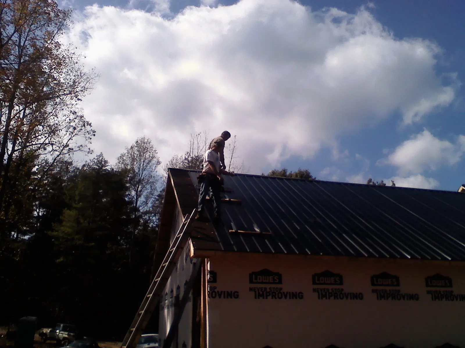 Roofer fastening dark metal panels high against a cloudy sky, from a Roof Inspection job in Mc Alpin