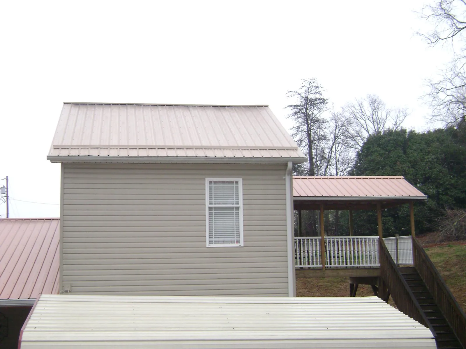 Tan metal roofs on a two story addition and attached porch, from a Roof Replacement job in Mc Alpin